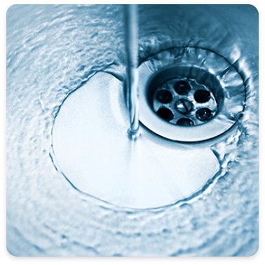 Water flows down a stainless steel sink drain, creating ripples in the water's surface. The drain's grate is visible, emphasizing the motion of the water as it disappears into the plumbing below.