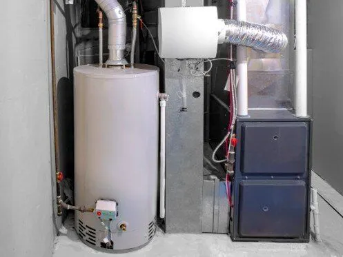 A water heater is installed in a utility room, accompanied by ductwork and pipes leading to a furnace. The space appears organized, with clearly marked components for plumbing and heating systems.