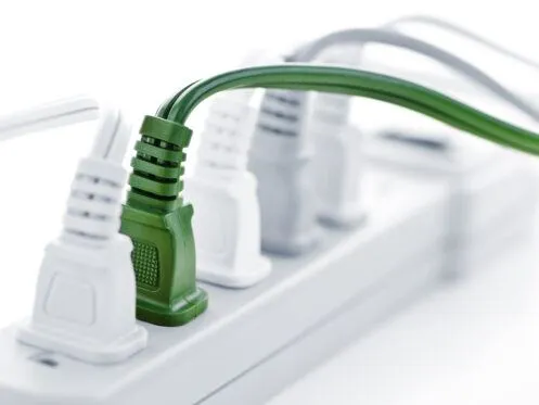 A close-up of a power strip shows several electrical plugs, with a distinctive green plug prominently inserted. The arrangement highlights the various cords, emphasizing their functionality against a light background.