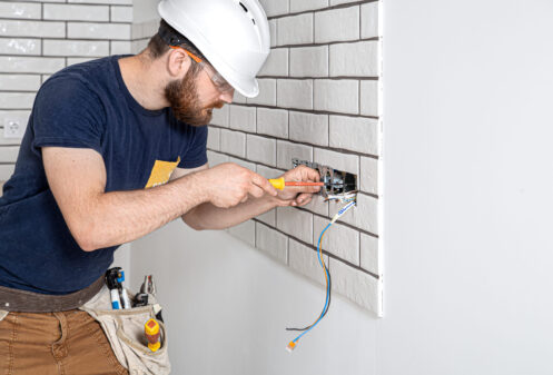 Electrician Builder at work, installation of sockets and switches. Professional in overalls with an electrician's tool. Against the background of the repair site. The concept of working as a professional.