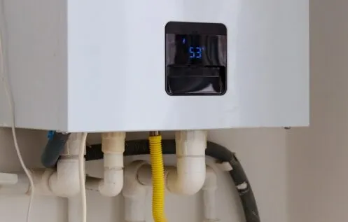 A tankless water heater is mounted on the wall, showing a digital display reading 53°F. Several pipes, including a yellow gas line, are connected beneath the unit.